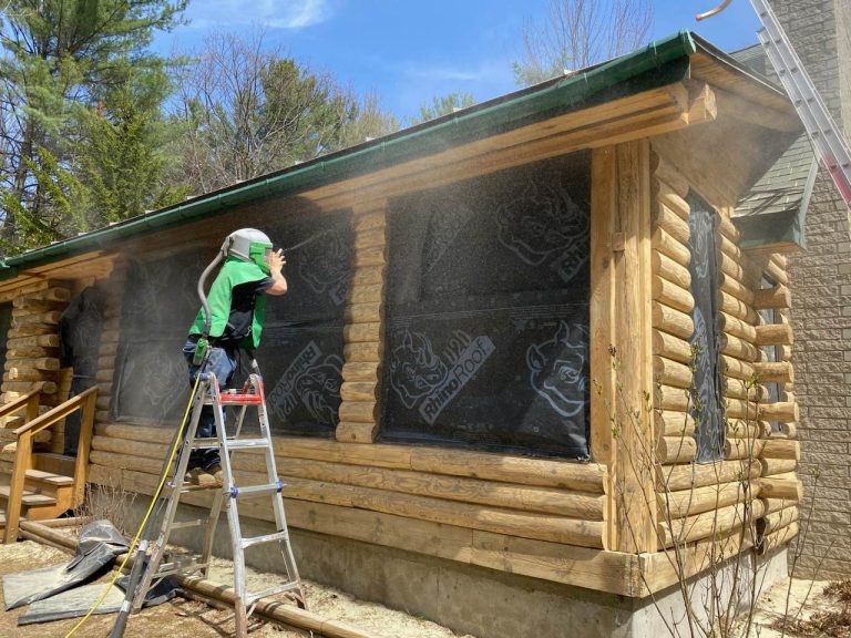 Worker preparing log home exterior with media blasting for chinking
